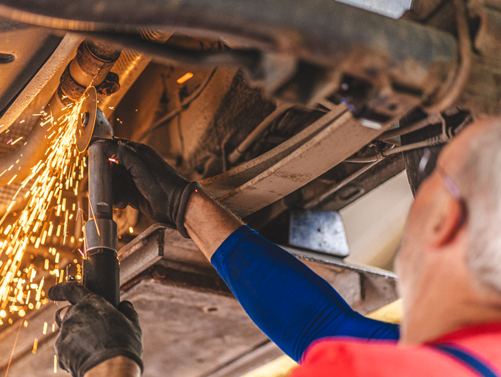 Werkstattmitarbeiter mit Trennschleifer unterm Auto auf Hebebühne. Werkstattmitarbeiter mit Trennschleifer unterm Auto auf Hebebühne.