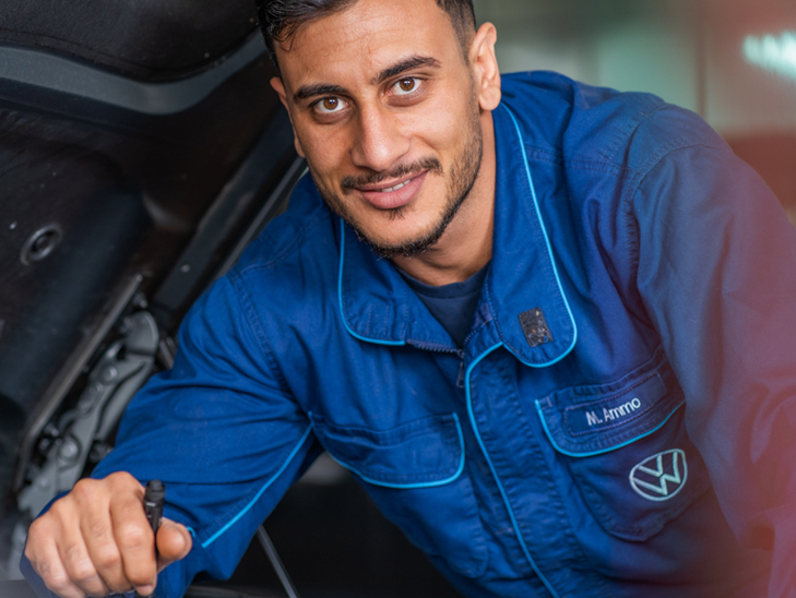 Kfz-Mechaniker steht vor offener Motorhaube und blickt in die Kamera. Kfz-Mechaniker steht vor offener Motorhaube und blickt in die Kamera.